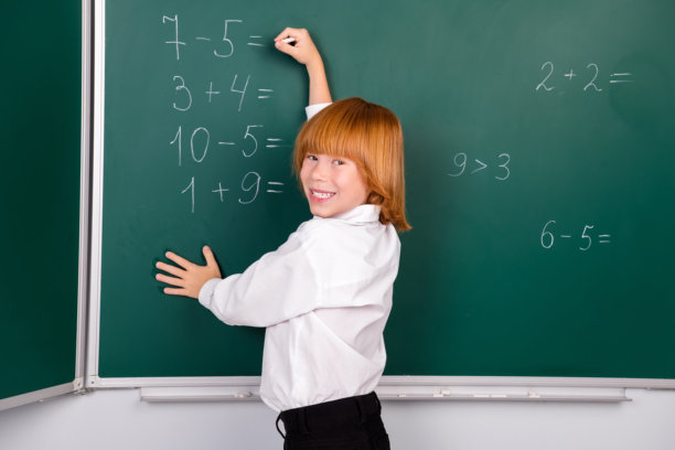 迷人的小学生男孩的照片写粉笔数学解决问题穿着时髦的统一教室黑板背景图片下载