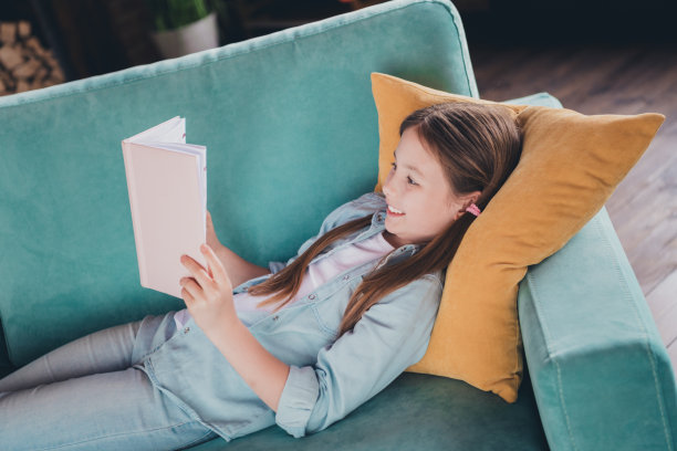 可爱的小女孩躺在沙发上看书，穿衬衫阁楼室内公寓室内的照片图片下载