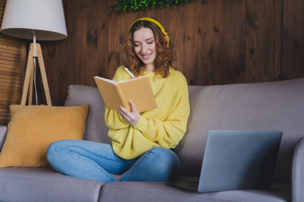 漂亮的年轻女子全身照片坐在沙发上学习笔记本穿着时尚的黄色毛衣现代的光舒适的室内平坦的室内图片下载