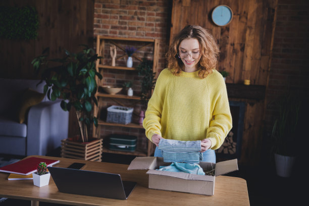可爱的年轻女士的照片在线包装包裹纸箱穿黄色毛衣女商人漂亮的阁楼舒适的光办公室图片下载