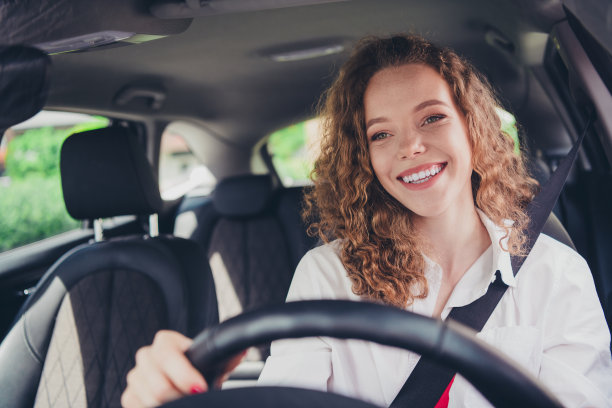漂亮可爱的女士穿着白衬衫微笑着开着租来的汽车在城市街道外的照片图片下载