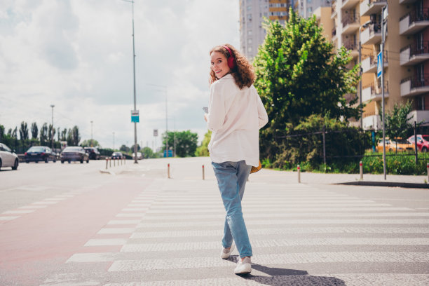 兴奋的梦幻女子的全尺寸照片，转身穿过马路，穿着白衬衫走在现代城市街道外图片下载