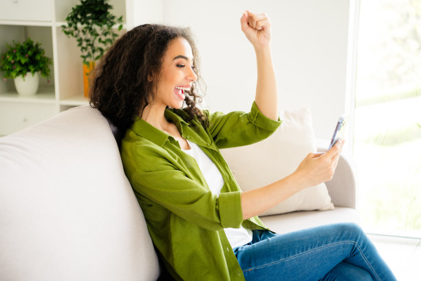 迷人的快乐女孩的照片，穿着卡其布时尚的衣服，坐在沙发上，拿着手机小工具，社交媒体流行周末室内图片下载