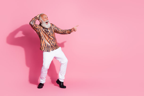 照片中，一个疯狂乐观的快乐男人穿着时尚的印花衣服，在粉红色的背景上展示了孤立的空间图片下载