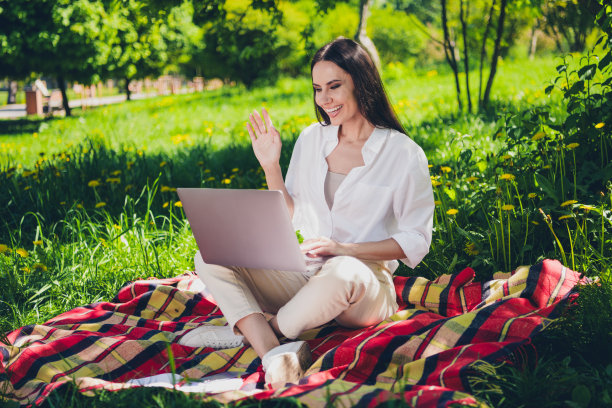 小女孩的全身照片坐在野餐格子毯子工作上网本视频通话挥手手穿着白色的衣服走在城市公园外图片下载