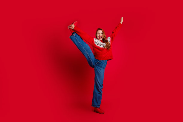 照片活泼的年轻红头发灵活的女孩穿着圣诞丑毛衣跳舞做分裂孤立的红色背景图片下载