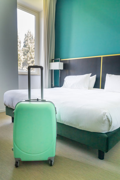薄荷绿色的手提行李箱放在酒店房间的床旁。旅行的概念。图片下载