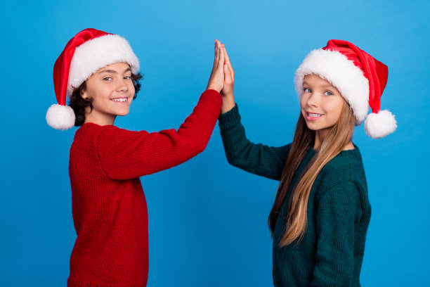照片中两个孩子击掌时穿着圣诞老人的服装，背景是孤立的蓝色图片下载