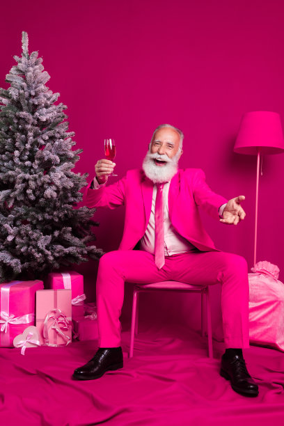 兴奋迷人的成熟的祖父的照片坐在椅子上举起香槟庆祝圣诞节穿粉红色的燕尾服靴子在房间内部图片下载