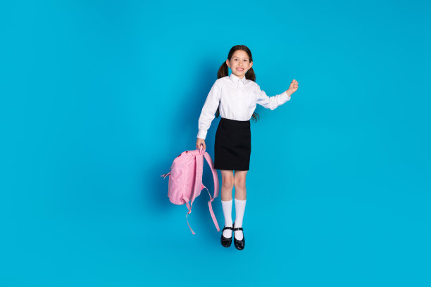 全尺寸照片的小学生穿着统一的跳跃背包孤立的蓝色背景图片下载