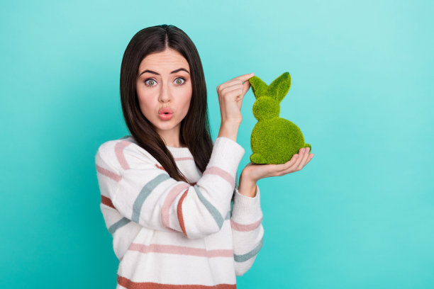 兴奋的少女可爱的女士抱着绿兔子送飞吻的照片，穿着条纹毛衣孤立的蓝色背景图片下载