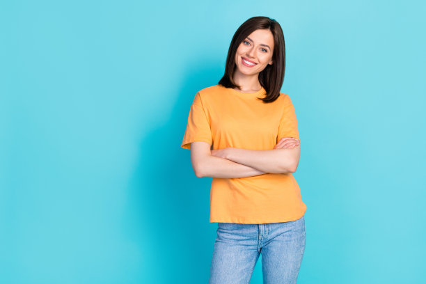 照片可爱漂亮开朗漂亮的女士手臂折叠穿着橙色时尚的衣服站空空间孤立在蓝色的背景图片下载