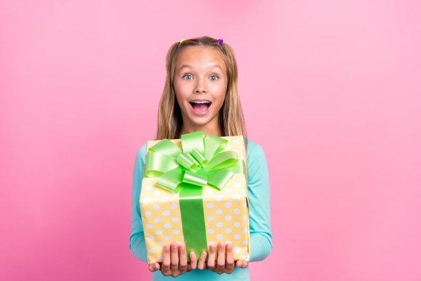 小女孩拿着新礼物的特写照片，兴奋的积极反应，现在孤立在明亮的粉红色背景上图片下载