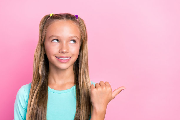 年轻漂亮可爱的少女小女人的特写照片，有牙齿的微笑，灿烂梦幻的样子，空白的空间手指点广告孤立在粉红色的背景图片下载
