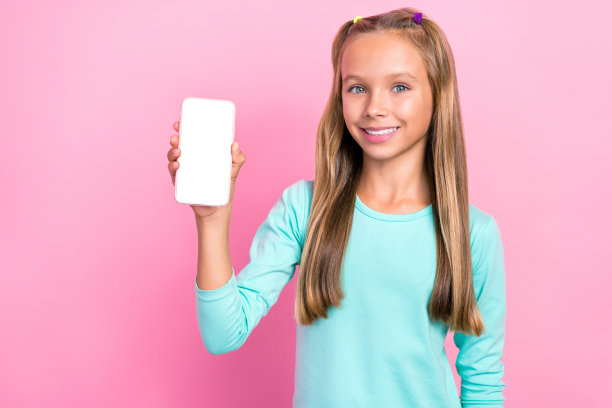 小学生的特写照片，穿着蓝色套头衫，露齿微笑，手持触摸屏，空白空间广告购物孤立在粉红色的背景图片下载