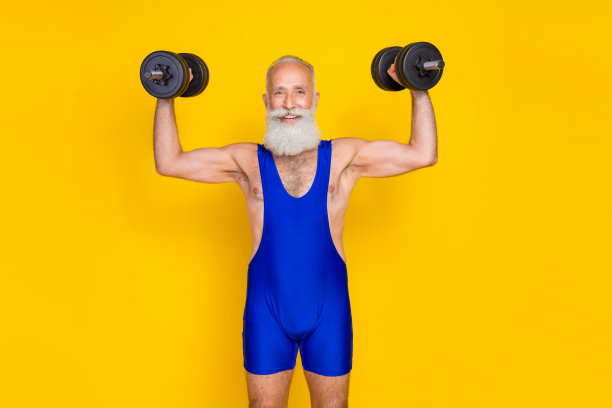 照片中开朗活泼的老人双手举哑铃孤立在黄色背景图片下载