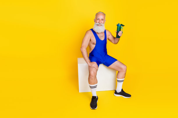 全长照片的积极运动的爷爷坐在平台上持有水瓶孤立的黄色背景图片下载