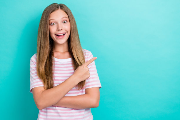 惊喜开朗的女孩的照片在绿松石色的背景上指指空白的空间提供隔离图片下载