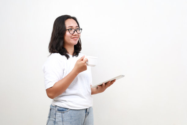 迷人的女商人一边喝着咖啡，一边用着电子平板电脑，站在白色的背景上，看着空白的空间图片下载