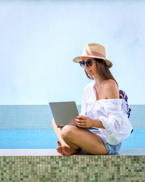 一个漂亮女人坐在泳池边用她的笔记本电脑图片下载