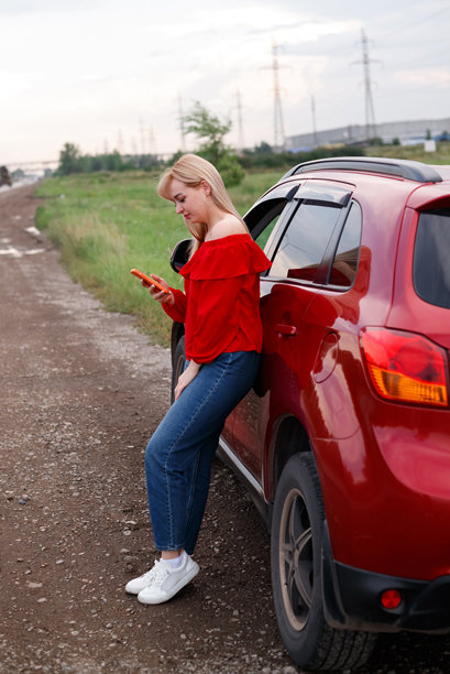 一个微笑的快乐乐观的年轻漂亮的女人站在车旁边在海滩上用手机聊天的照片。图片下载