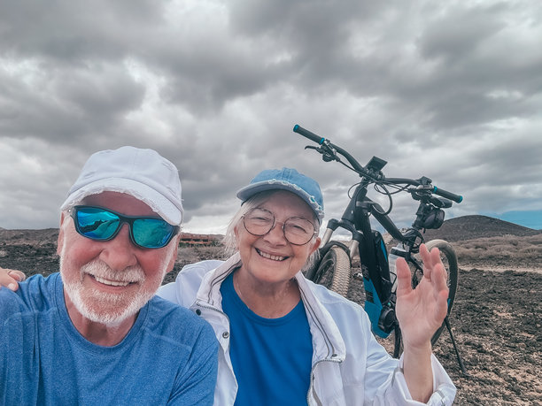 一对快乐活跃的老人夫妇骑着电动自行车在乡村拍一张记忆照片，拥抱着看着相机享受退休后健康的生活方式。水面上地平线图片下载
