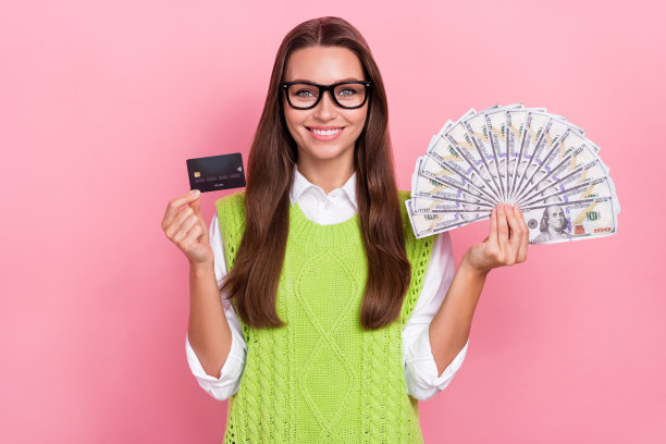 照片开朗乐观满意的女商人持有信用卡很多钱开语言课程学校孤立的粉红色背景图片下载