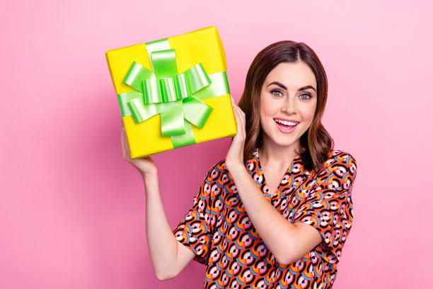 年轻的时髦女士的照片穿着旧的复古印花衬衫夏天的礼物拿着礼物猜摇盒子里面什么孤立在粉红色的背景图片下载