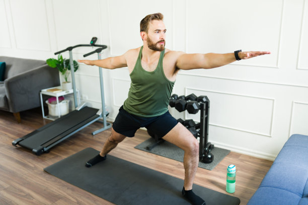 穿着运动服的男子在家庭健身房锻炼时以战士姿势练习瑜伽图片下载