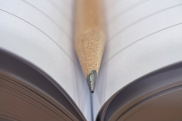 铅笔在笔记本上。一张特写，一只木制铅笔搁在一本打开了几页的笔记本上。图片下载