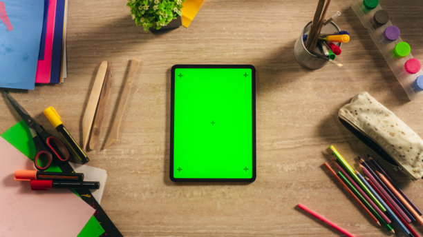 平板电脑的俯视图与垂直模拟绿屏Chromakey显示与运动跟踪器躺在设计师的桌子旁边的彩色铅笔，标记，艺术供应工具的插画家图片下载