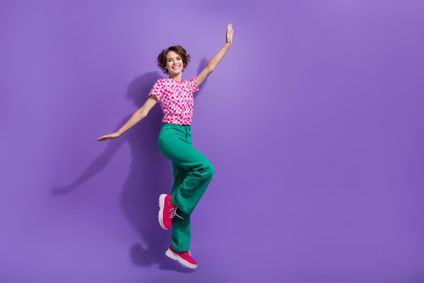 大喜大喜的无忧无虑的女人穿着印花t恤跳跃手像翅膀孤立的紫罗兰色背景照片图片下载