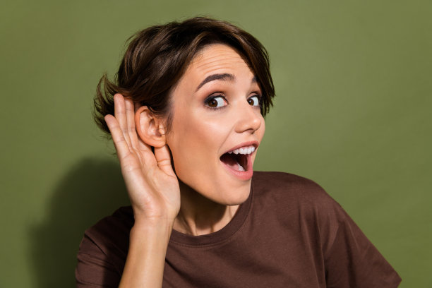 照片欣喜若狂的女人与鲍勃头发穿着棕色t恤，手放在耳朵听秘密销售公告孤立的卡其色背景图片下载