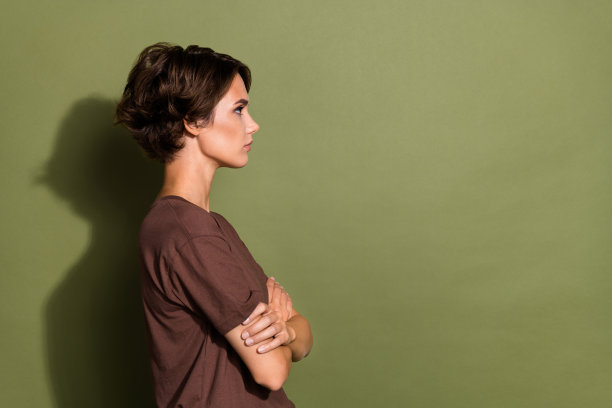 侧面侧面照片的漂亮女人与鲍勃发型穿着t恤手臂交叉看空空间孤立的卡其色背景图片下载