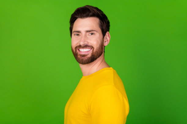侧面侧面照片的快乐男子与时尚的胡子，穿着黄色衬衫，牙齿微笑孤立在充满活力的绿色背景图片下载