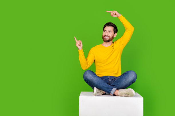 帅小伙的全身照片点看空旷的空间坐立方体穿着时髦的黄色服装孤立在绿色的背景图片下载