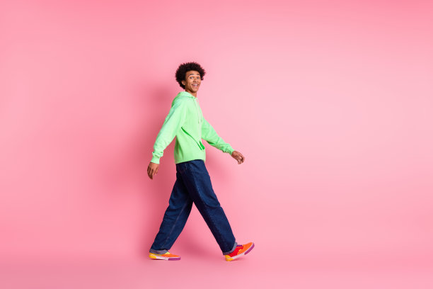 漂亮的年轻人的全尺寸照片走空空间穿绿色卫衣孤立在粉红色的背景图片下载