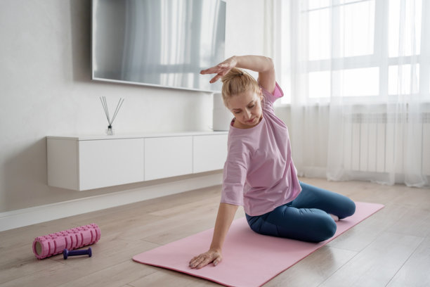 在一间现代化的客厅里，一位女士正在粉红色的垫子上做瑜伽，专注于她的练习图片下载