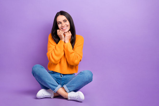 开朗可爱的女士的全身照片，穿着舒适的衣服，坐在地板上，看着紫色背景上孤立的空间图片下载