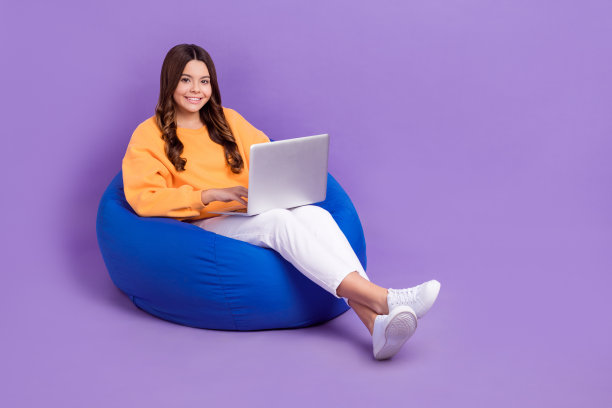 开朗的女士全身照片穿橙色运动衫豆袋在线课程小工具空的空间孤立的紫色背景图片下载