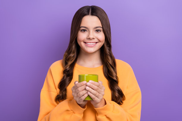 可爱的开朗和平的女孩的照片，露齿微笑的手拿着热巧克力杯孤立的紫色背景图片下载