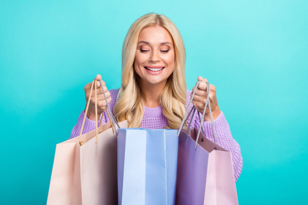 照片成熟的年龄有趣的金发女士看猜猜什么在她的购物袋理想的礼物衣服孤立的青色背景图片下载