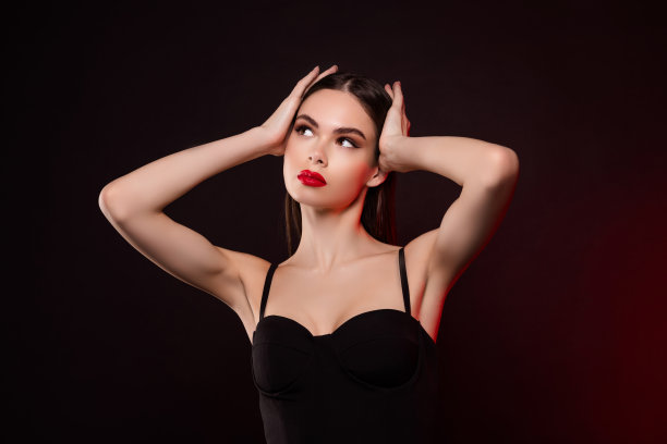 照片中的女士穿着黑色的裙子，触摸头发，调整发型，看起来空白的空间孤立的黑暗霓虹色背景图片下载