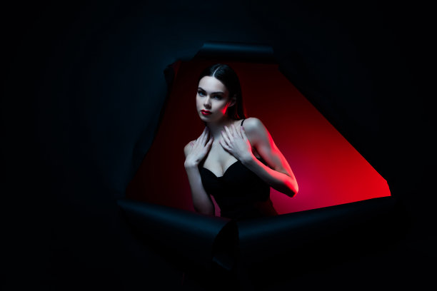 照片中的女士穿着晚礼服，站在洞里摸胸，感觉诱人的孤立的黑暗背景图片下载