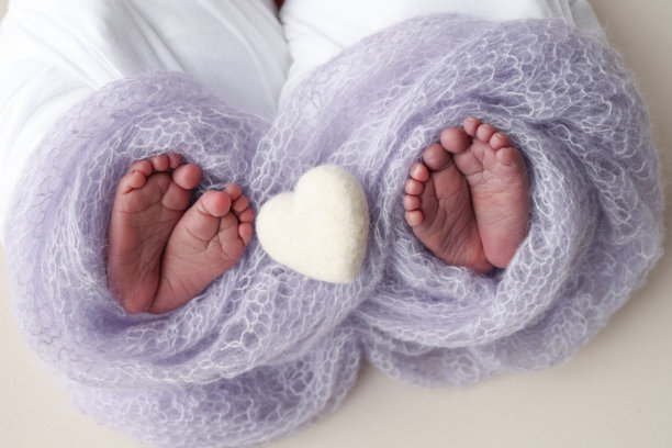 新生双胞胎的脚。两双婴儿的脚裹在淡紫色的蓝毯子里。白色编织的心。近距离观察新生儿的脚趾、脚跟和脚。新生儿双胞胎兄弟、姐妹。工作室微距照片。图片下载
