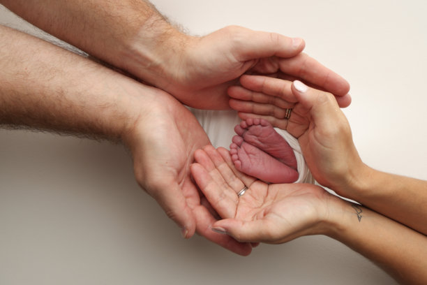 父母的手掌。父亲和母亲用白色的毯子抱着新生儿的脚，白色的背景。新生儿的脚握在父母手中。脚，脚跟和脚趾的照片图片下载