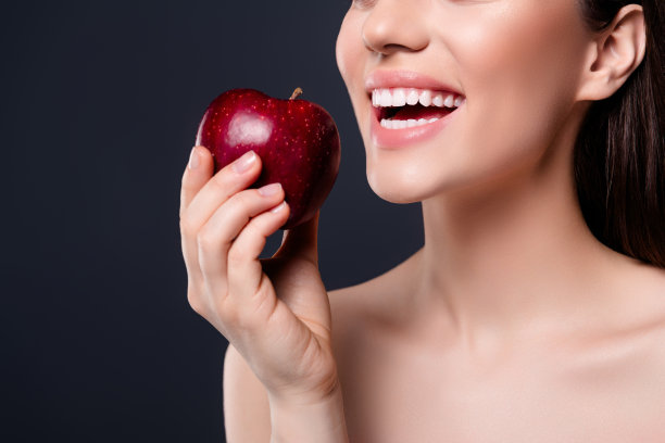 裁剪照片的女孩与健康的白色牙齿咬水果孤立的深色背景图片下载