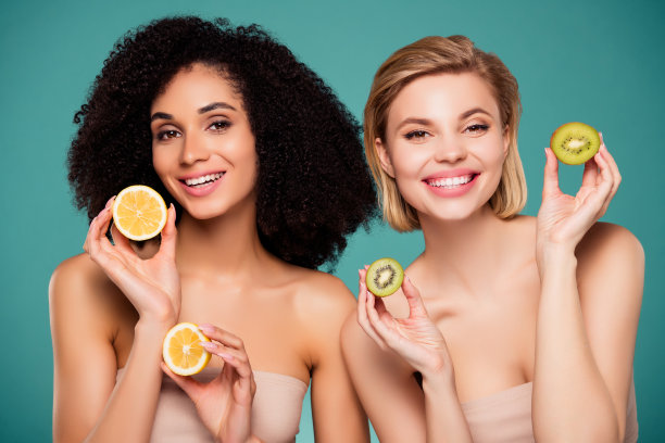 照片中微笑的两个女孩拿着水果片猕猴桃柠檬孤立的青色背景图片下载