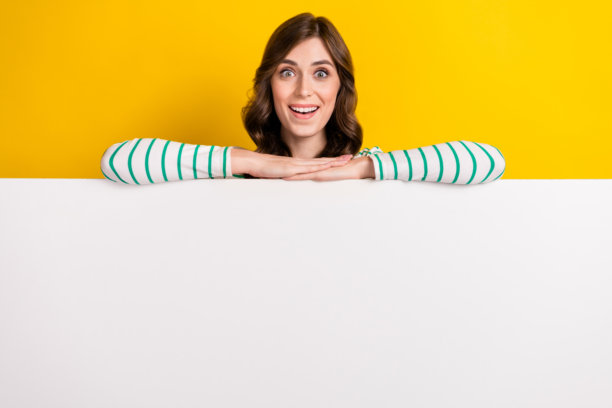 照片中，一个满意的印象深刻的女人，有着卷曲的发型，穿着条纹衬衫，在黄色背景的广告牌上抱着手臂图片下载