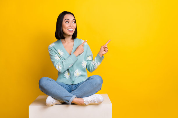 正面印象深刻的女孩蓝色开衫的全长照片表明空白空间坐在立方体孤立的黄色背景图片下载